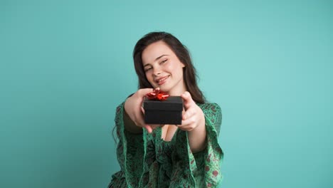 Happy woman giving gift box and looking at camera in blue studio