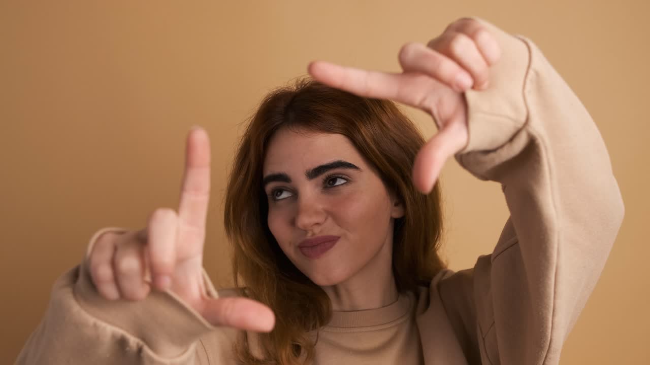 Cheerful woman showing frame gesture with fingers in studio