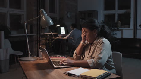 woman working late at night in an office, showing signs of fatigue