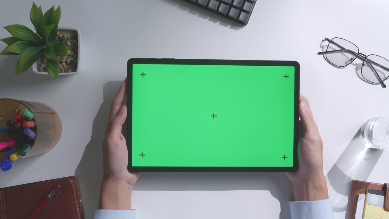 верхний вид ноутбука с макетным зеленым экраном chromakey на деревянном офисном столе рядом с ноутбуком с ручками, очками и стаканом воды.