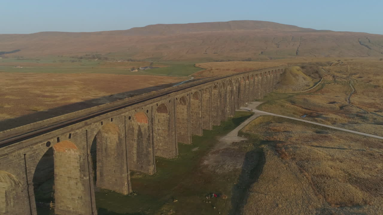 un dron aéreo disparó a lo largo del puente del tren del viaducto ribblehead en un impresionante amanecer con largas sombras en verano en los valles de yorkshire, inglaterra, reino unido, con 3 picos de la montaña whernside en segundo plano.