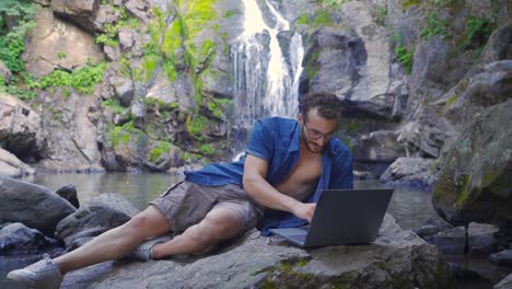 trabajando en la computadora portátil en la cascada en el bosque.