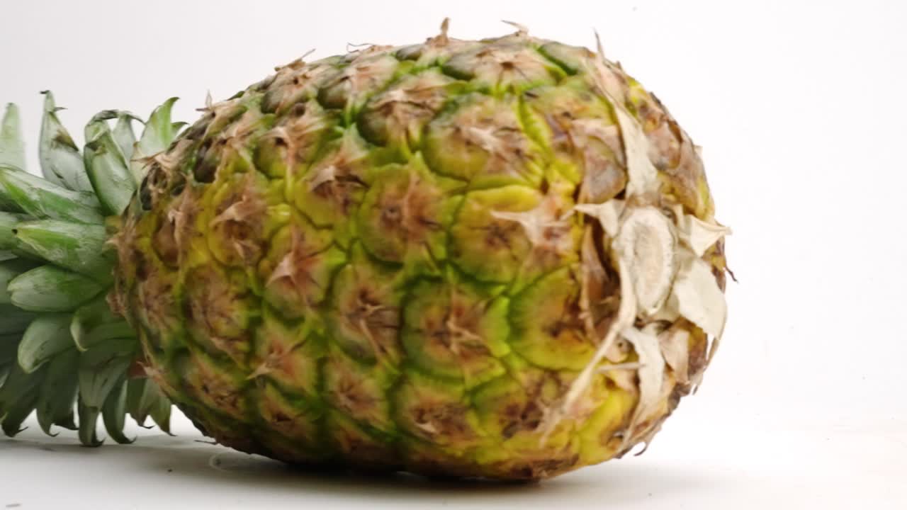 노란색 열대 파인애플 전체가 흰색 테이블 위에 원을 그리며 천천히 움직입니다.