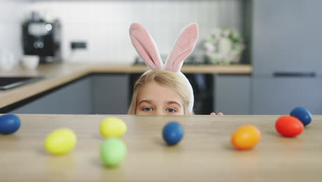 child hiding behind counter looking at easter eggs