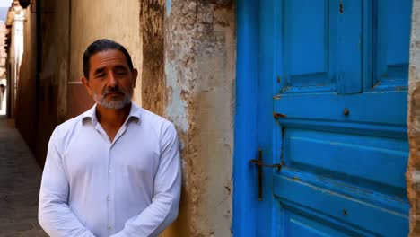 man leaning against a wall in a narrow alleyway with a blue door