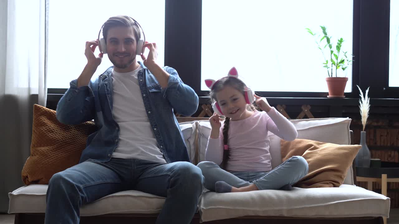 Charming girl and her handsome young dad in headphones are listening to music