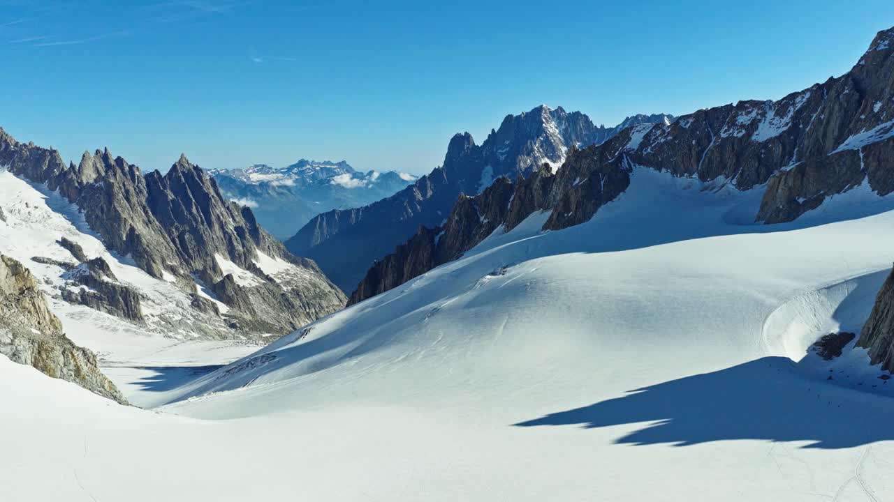 Cinematic aerial view over pristine snowfield framed by dramatic rugged alpine peaks in Chamonix, France. Ideal for travel, winter, nature and adventure themes