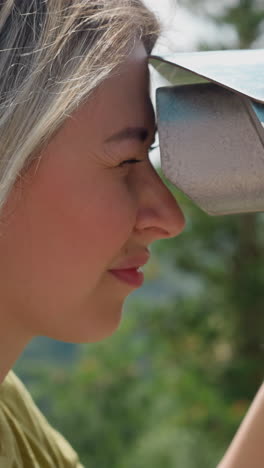 una mujer sonriente gira la rueda de ajuste mirando a través de poderosos binoculares en el punto de vista en el complejo verde en un soleado día de verano de primer plano en cámara lenta