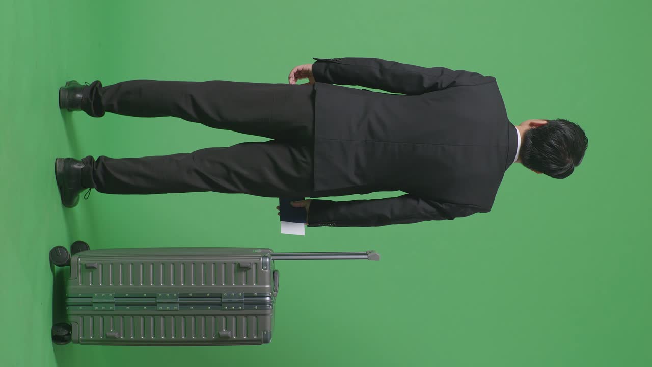 짐을 들고 여권을 들고 초록색 스크린 배경 스튜디오에 서있는 동안 주변을 둘러보는 사업가 여행자의 전체 뒷면