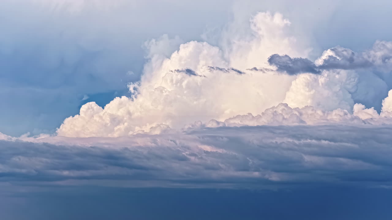A stunning aerial timelapse captures the movement of majestic, fluffy white cumulus clouds building and billowing above a layer of darker clouds in a beautiful blue sky