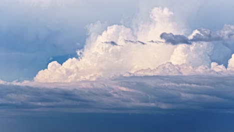 a stunning aerial timelapse captures the movement of majestic, fluffy white cumulus clouds building and billowing above a layer of darker clouds in a beautiful blue sky