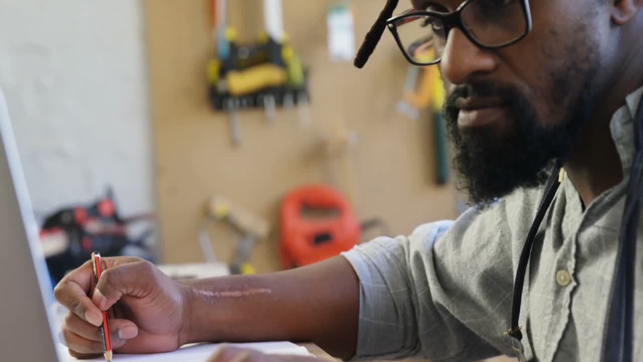 Carpenter writing in notepad while using computer 4k