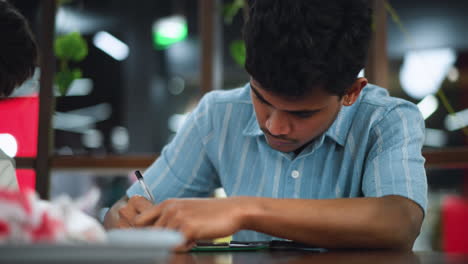 bent profile view of young man in blue shirt intensely sketching on paper with focused expression swift hand motion capturing artistic technique under soft studio lighting highlight creative process