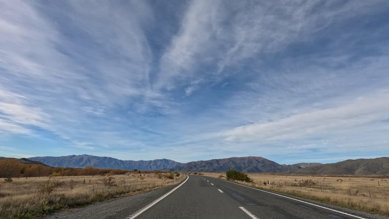 A serene drive on a rural road in Queenstown, New Zealand, showcasing expansive skies and autumn foliage under soft daylight