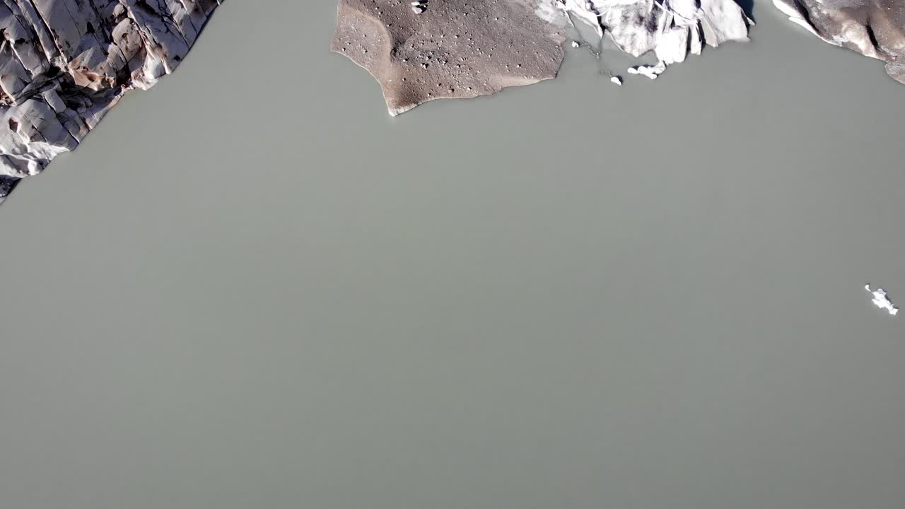 Aerial view of Rhone glacier near Furka mountain pass at the border of Valais and Uri in Switzerland with a pan up from the icebergs in the glacial lake up to the mountain peaks