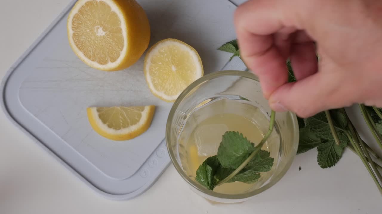 Freshly made lemonade with mint leaves and lemon slices next to an iced glass