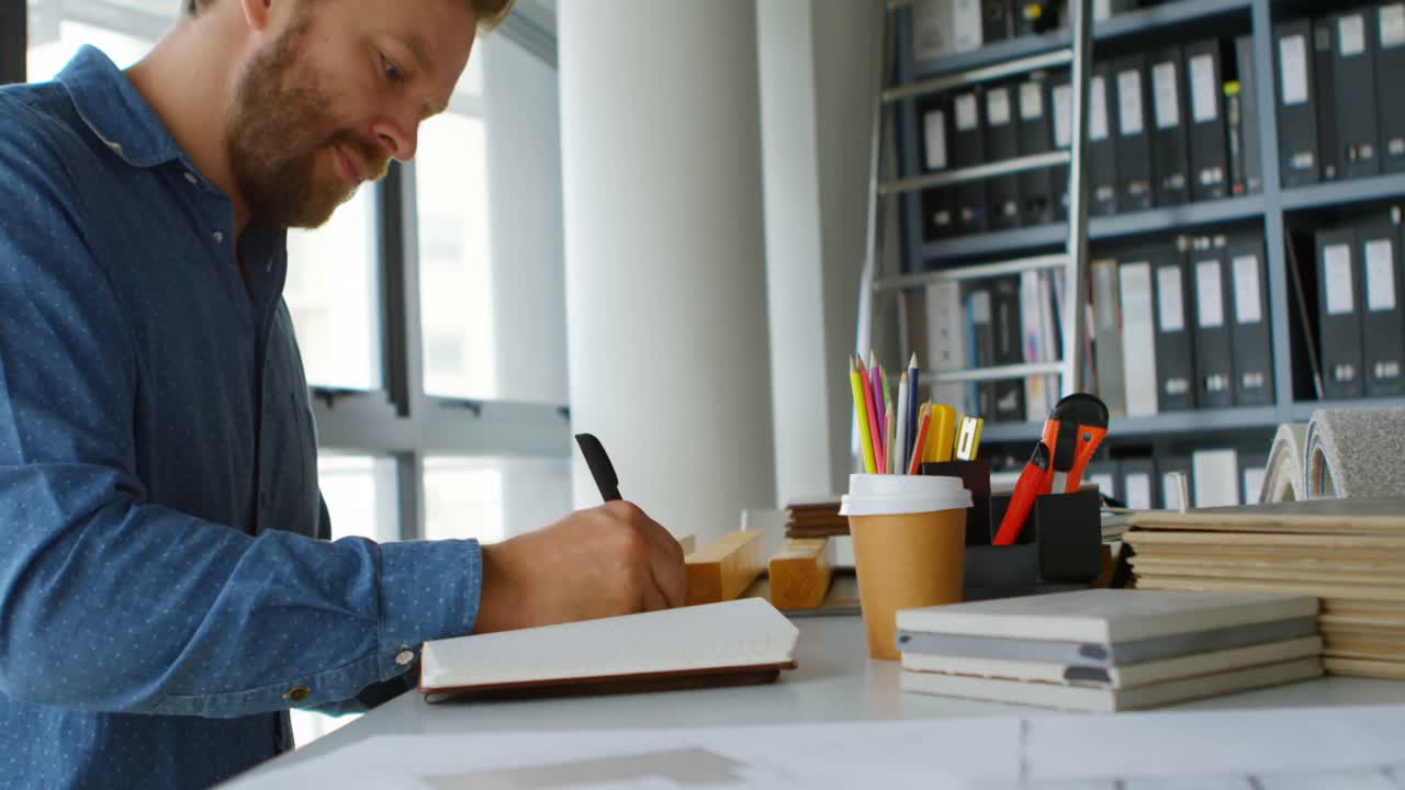 arquitecto masculino escribiendo en un diario en el escritorio 4k