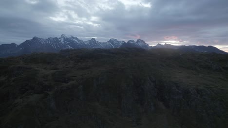 aerial view over a mountain revealing the dramatic sunset above a snowy range - rising, drone shot