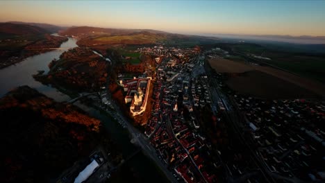 Steady-descending-FPV-shot-towards-castle-Melk,-capturing-beautiful-evening-lights-in-late-fall