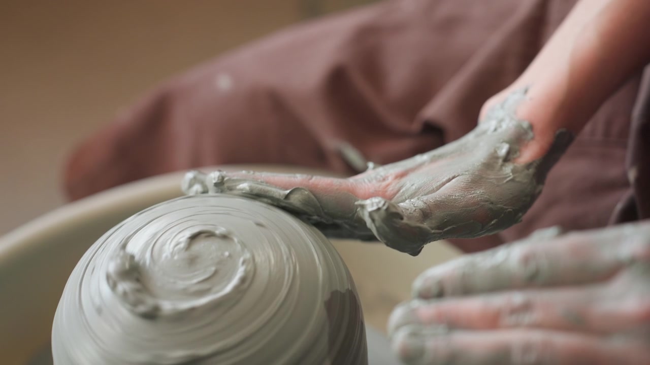 Potter forming bowl with hands. Wheel spins as hands mold wet clay. Creating spiral textures on wet clay with steady hands. Potter skillfully shapes spinning clay into textured bowl in studio