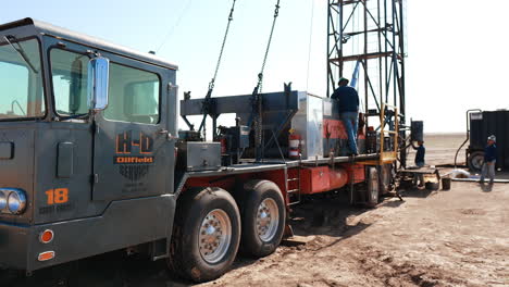 special truck with drilling equipment on. a group pf men wearing protective helmets arrange the oil derrick.