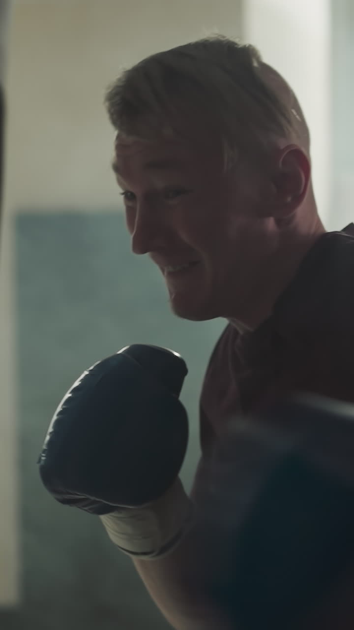 hombre feliz golpea una bolsa pesada rápido en el centro deportivo. deportista sonriente golpea el equipo por los brazos en un gimnasio nebuloso en cámara lenta. mejoramiento del estilo de combate