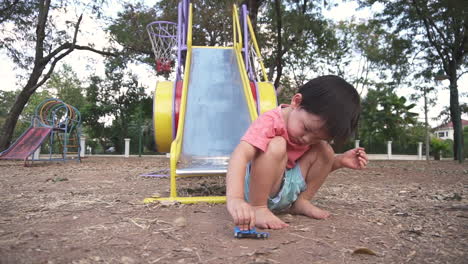 east asian toddler  having fun playing with a toy car or truck sitting on the ground of an outdoor  park