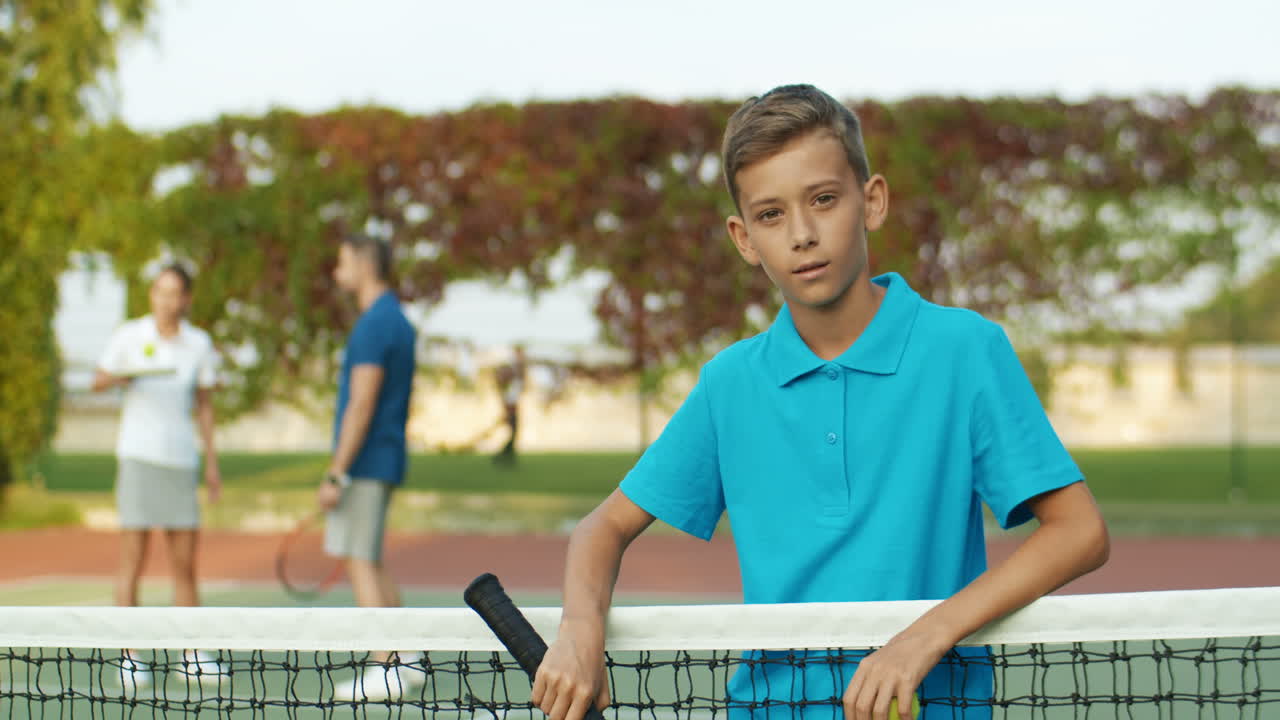 여름에 야외 코트에서 테니스를 치는 방법을 십대 아들에게 가르치는 남자