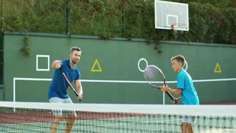 hombre enseñando a su hijo adolescente a jugar tenis en una cancha al aire libre en verano