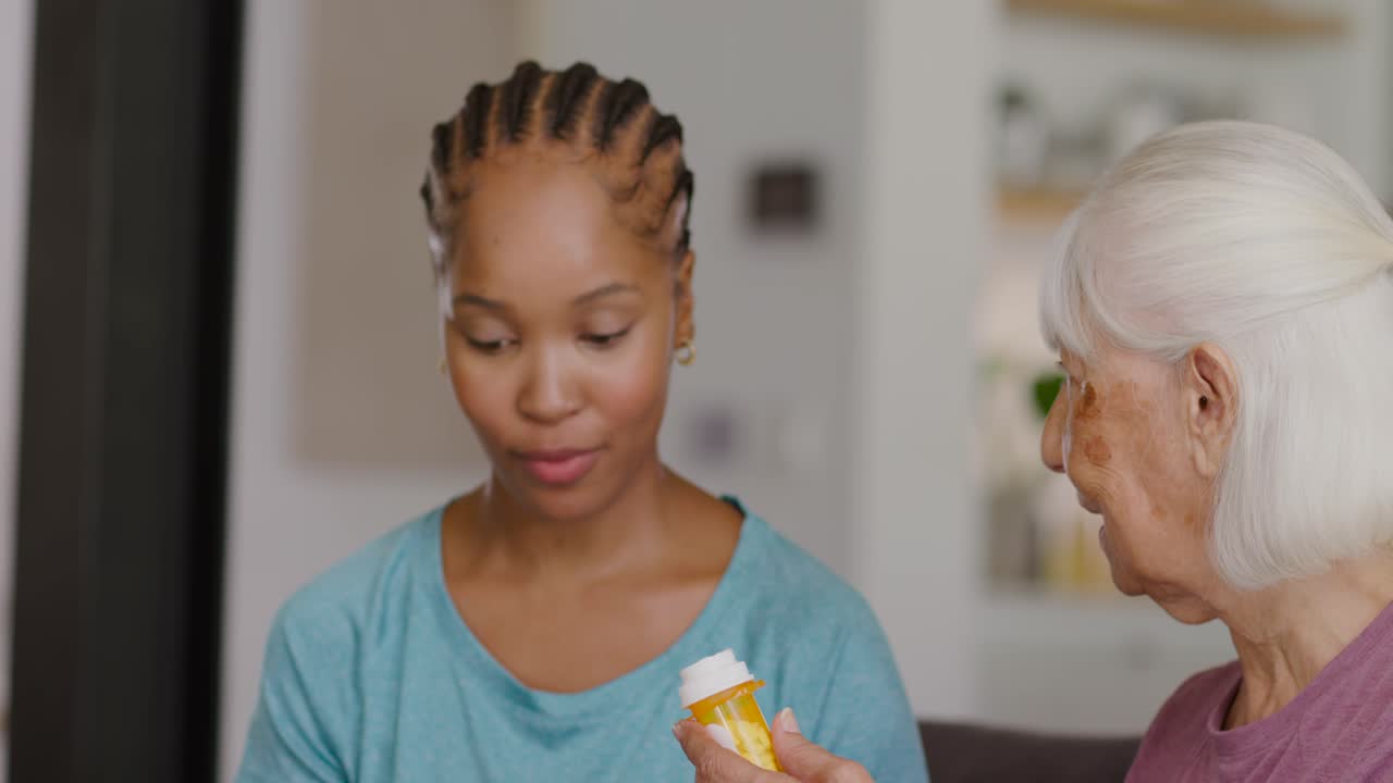Diverse women on couch, senior showing pill bottle, caregiver checking tablet, verifying meds