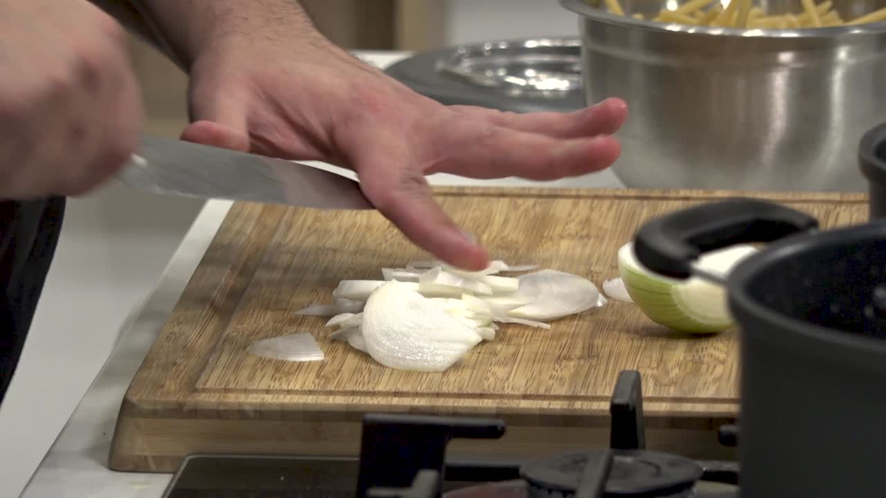 Capsicum, onion, and garlic are skillfully chopped on a wooden board as the chef preps for an enticing pasta recipe in a contemporary kitchen ambiance.