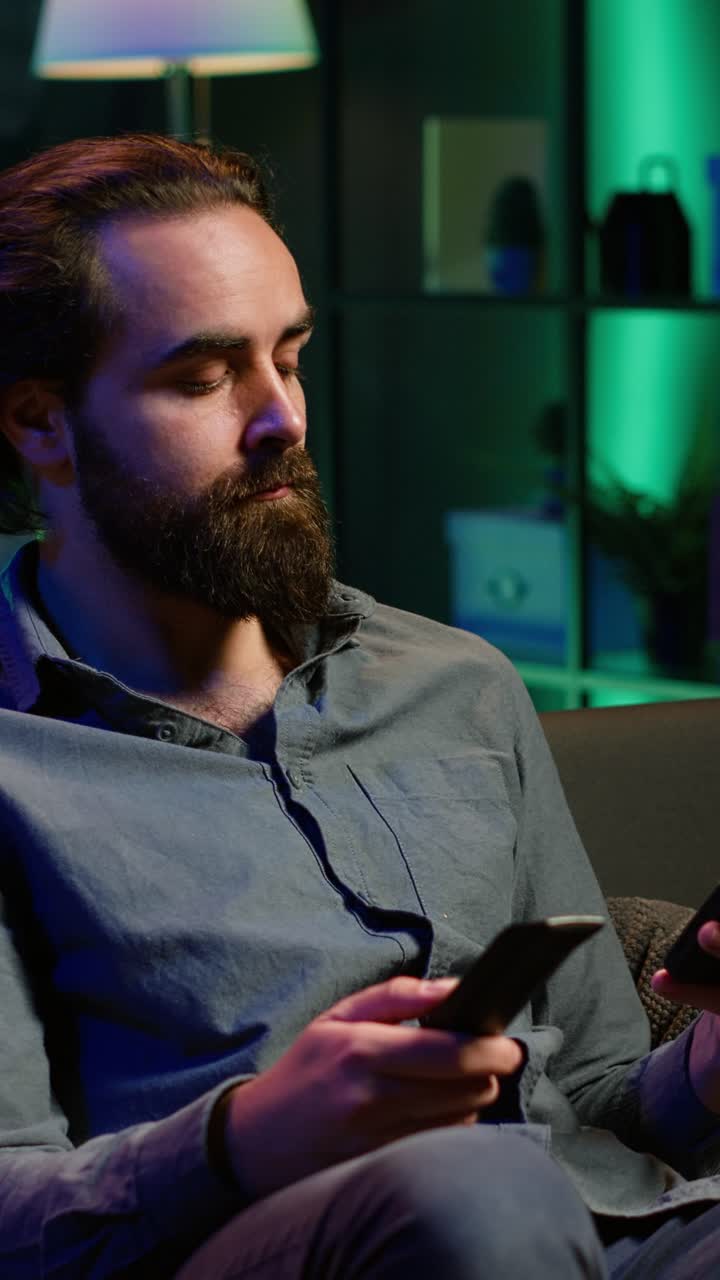 Vertical video Person watching TV, texting friend on mobile phone, holding remote control