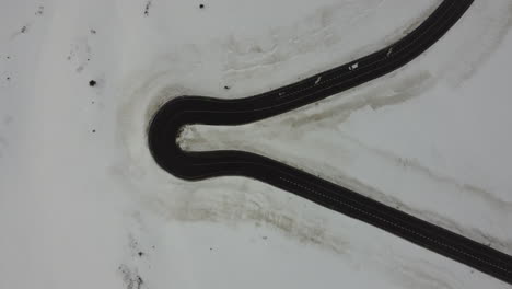 vista aérea de arriba hacia abajo de un automóvil blanco que conduce un camino cerrado que gira contra el paisaje nevado