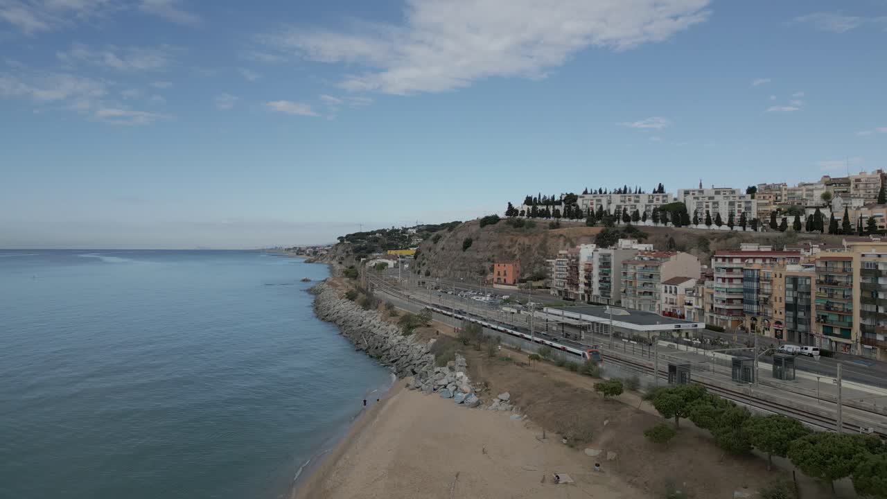 Volo di drone aereo sopra la stazione ferroviaria sul mare, litorale collinare di Arenys de Mar, Catalogna, Spagna, spiaggia, skyline, viale e architettura cittadina
