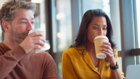 mature male businessman brings takeaway coffee for female colleague as they have meeting with laptop