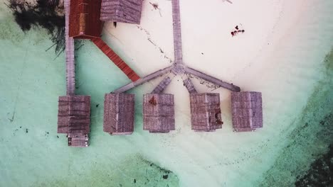 Nus-Raja-Resort-with-overwater-bungalows-in-the-Raja-Ampat-island-chain-Indonesia-with-people-on-beach,-Aerial-top-view-lift-shot