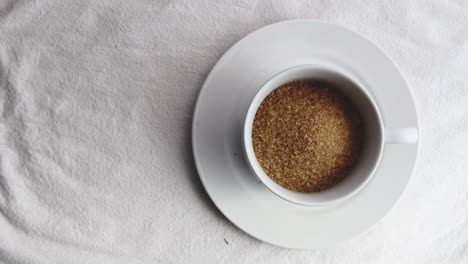 Raw-brown-sugar-in-white-ceramic-tableware-on-white-mat