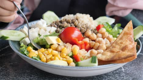 close up of a delicious and healthy salad with chickpeas, lentils, quinoa, corn, tomato, cucumber, cheese, red pepper, and tortilla chips