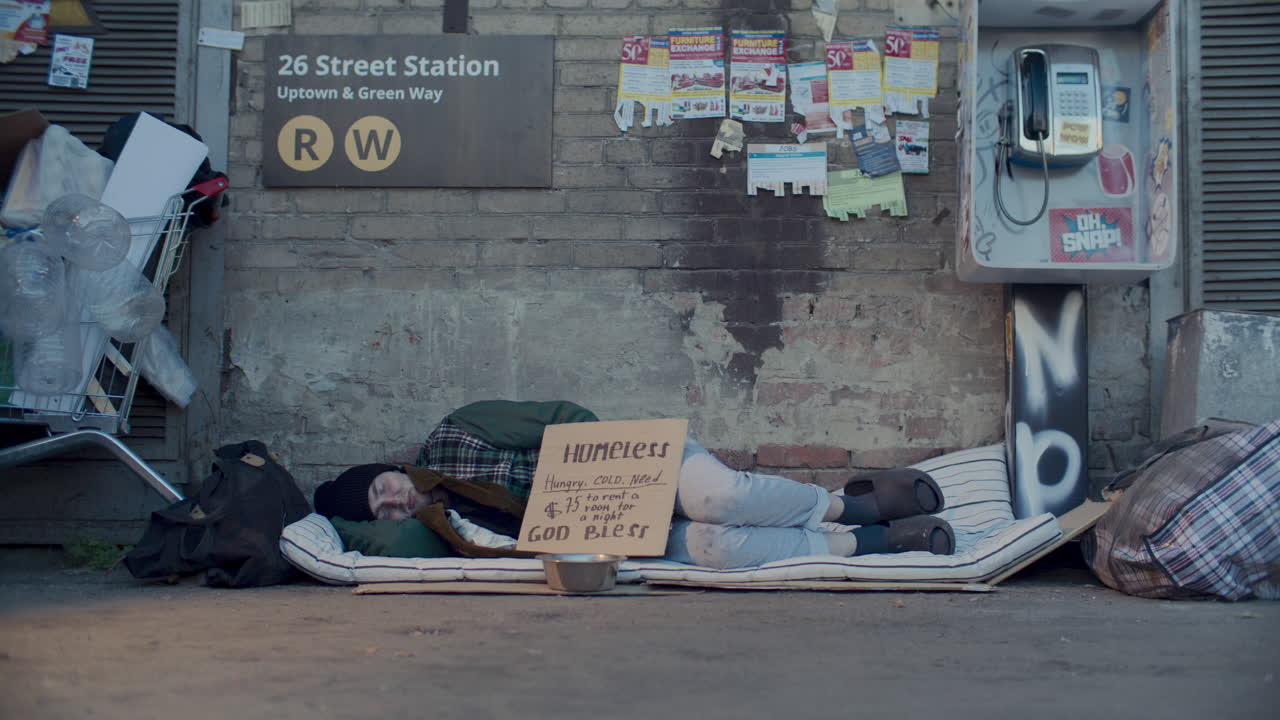 Homeless Man Sleeping on Worn Mattress below Subway Sign