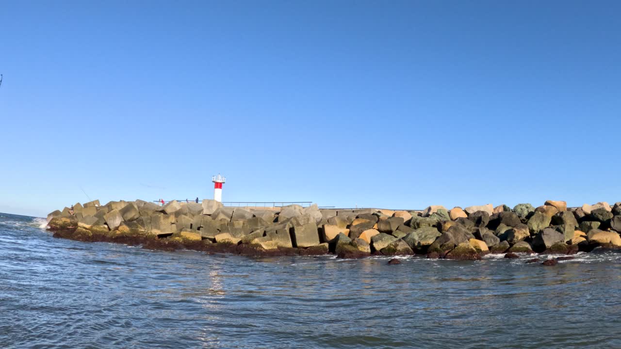 밝은 하늘 아래의 등대와 바위가 있는 해안