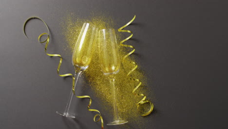 video of two champagne flute glasses with gold streamers and glitter on black, with copy space