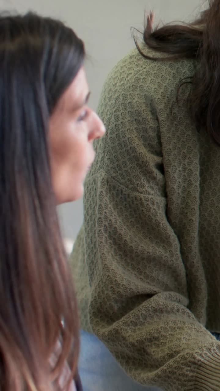 Mulher à esquerda conversando com um colega de trabalho, esclarecendo um plano, com suéter verde-oliva e relógio visíveis.