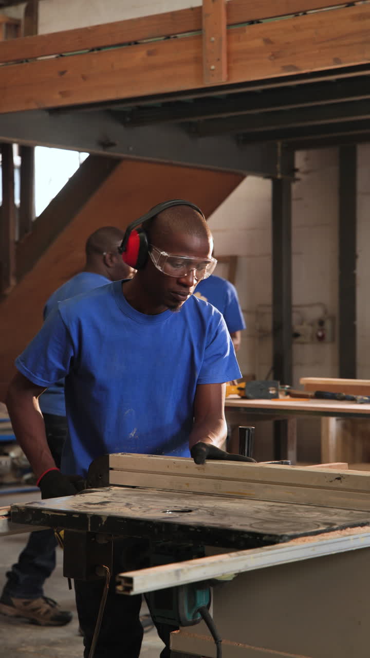Vertical video: African American male carpenter feeding board at saw checking accuracy in workshop