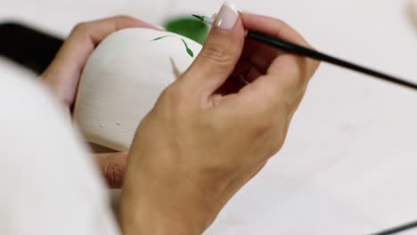 close up of the hands of an artist painting a drawing on the pottery in a workshop