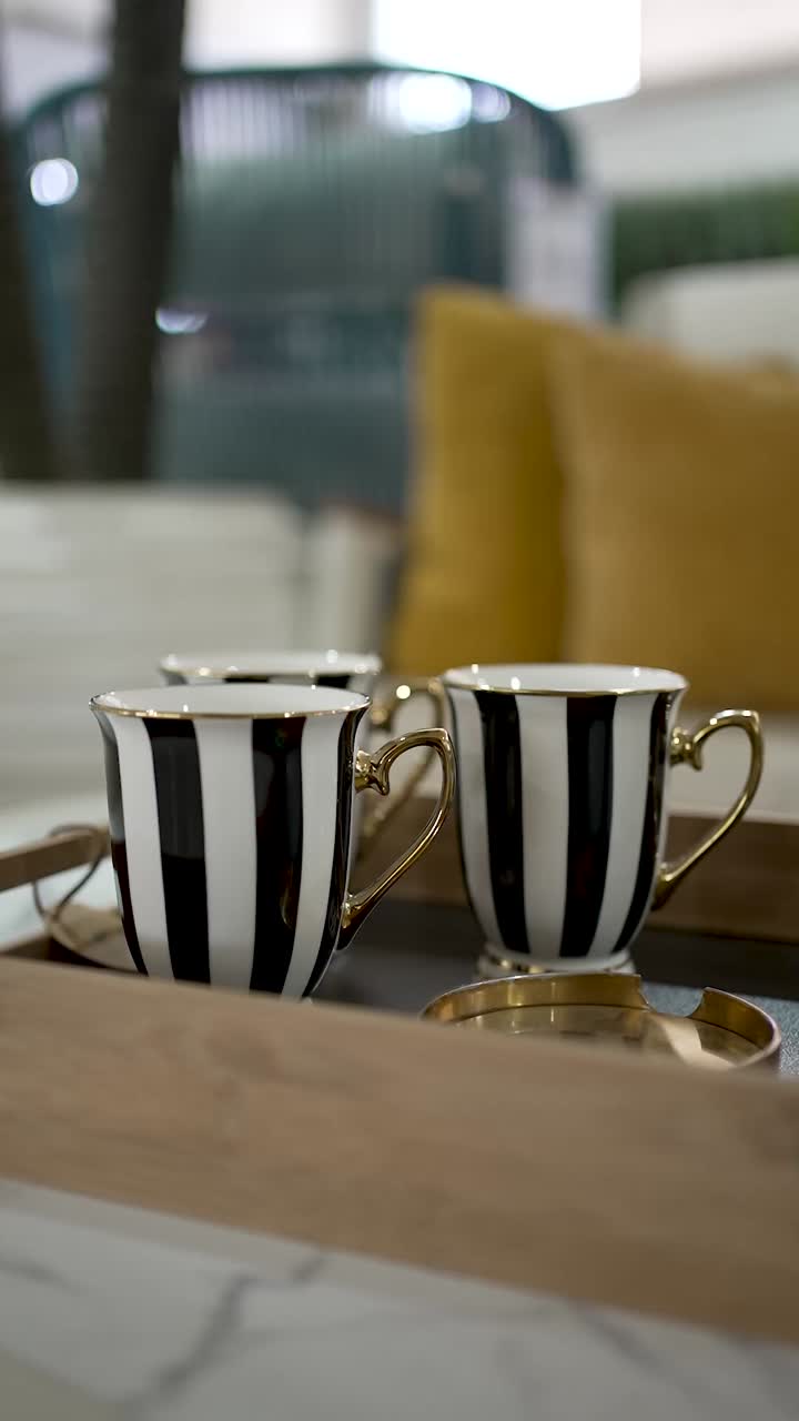 Three beautiful striped cups sit on a wooden tray, surrounded by soft cushions that create a warm and inviting atmosphere. Perfect for a relaxing moment with friends