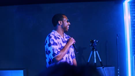 black african male man artist singer rapper showman performs performs concert party and sings on the club stage in dark scenery with neon lights blue theme