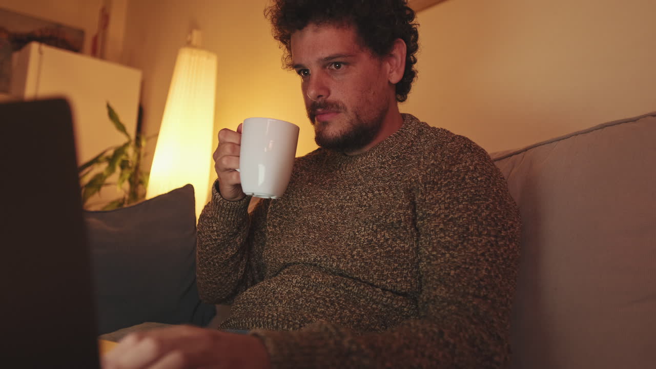 Man drinking coffee and using laptop at night