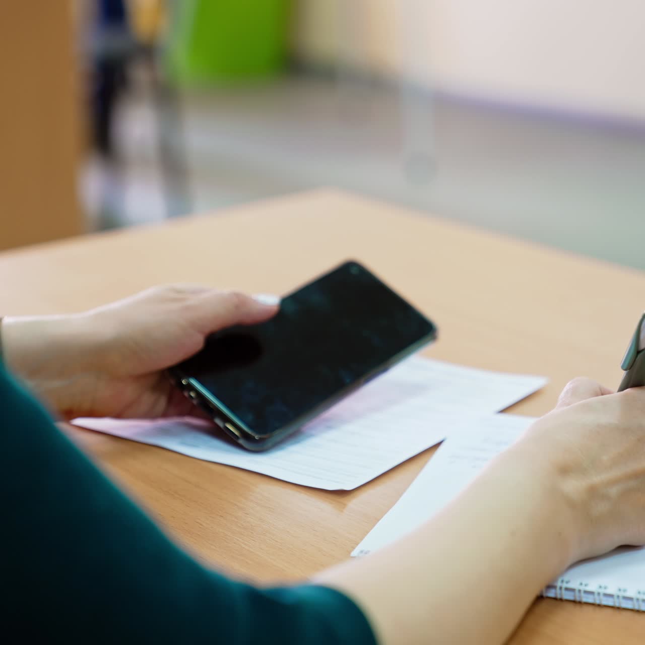 Unrecognized woman taking notes into paper notebook. Woman holding a phone in another hand. Blurred backdrop
