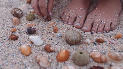 Nahaufnahme-Der-Füße-Einer-Frau,-Die-Muscheln-Am-Strand-Sammelt-Und-Die-Wunderschöne-Natürliche-Vielfalt-Genießt,-Die-Muster-Auf-Sand-Formt