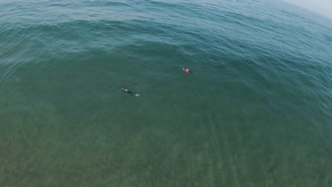 Aerial-orbit-around-bodyboarders-wearing-wetsuits-in-clear-ocean-water